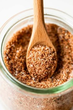 a wooden spoon in a glass jar filled with ground cinnamon and seasoning flakes