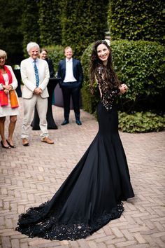 a woman in a long black dress standing on a brick walkway next to other people