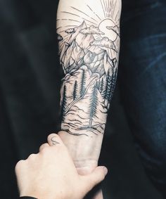 a person is holding their arm with a mountain scene tattoo on it's sleeve