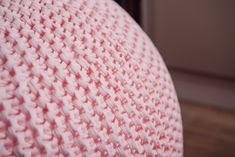 a pink knitted cushion sitting on top of a wooden floor