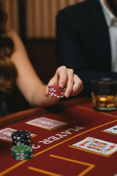 a man is playing cards at a casino table with two women in the back ground