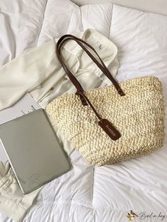 a white bed topped with a handbag next to a laptop computer