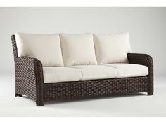 a wicker couch with white pillows on it's arm and backrests