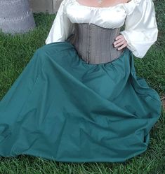 a woman sitting on the grass wearing a green skirt and white blouse with long sleeves