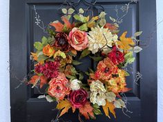 a wreath made out of fake flowers is hanging on the front door with leaves and branches