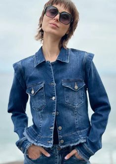 a woman standing on the beach wearing a jean jacket with her hands in her pockets