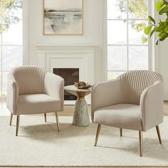 two beige chairs sitting next to each other in front of a fire place with a painting on the wall