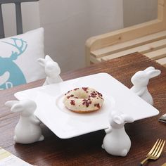 a white plate topped with a donut on top of a wooden table next to a fork and knife