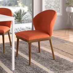 two orange chairs sitting on top of a carpeted floor next to a white table