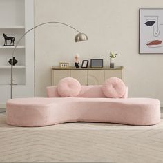 a pink couch sitting on top of a white floor next to a lamp and book shelf