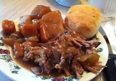 a white plate topped with meat and potatoes on top of a table next to a roll