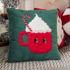 a green pillow with a red mug and candy cane on it