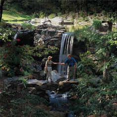 two people standing on rocks in front of a waterfall