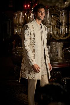 a man standing in front of a chandelier wearing a white and gold outfit