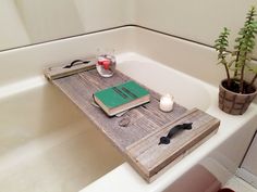 a bathtub with a book, candle and plant on the tray next to it