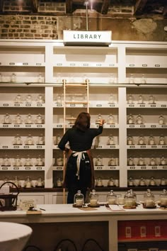 a woman standing in front of a shelf filled with jars