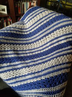 a blue and white crocheted blanket sitting on top of a couch next to a book shelf