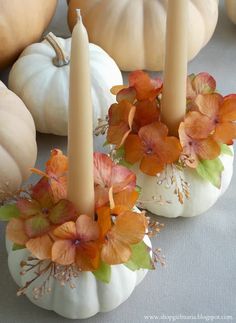 three candles with flowers on them sitting in front of pumpkins and other fall decorations