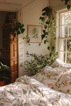 an unmade bed with plants hanging from the ceiling