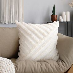 a white pillow sitting on top of a couch next to a vase and potted plant