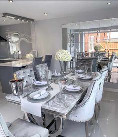 a dining room table is set with silver chairs and white plates on the dinner table