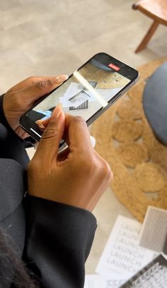 a person holding a cell phone in their hand while sitting at a table with papers on it