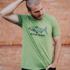 Hook, line, and sinker - the Montana Fish Unisex Tee in heathered green is a must-have for any outdoor enthusiast! With a playful nod to the state's abundant aquatic life, this tee is both stylish and comfortable (just like a day on the lake). Reel it in today! This Montana fish tee is a unisex fit. Female model is wearing a size small. Male model is wearing a large52/48 cotton/polyester Body Length 28 29 30 31 32 Chest Width (Laid Flat) 18 20 22 24 26 A Montana Scene Original Design. Printed in Hook Line And Sinker, Day On The Lake, Fit Female, Aquatic Life, Outdoor Enthusiast, Female Model, Store Fronts, Male Model, Original Design