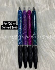 three pens sitting next to each other on top of a white fur covered surface with the words mermaid tears written above them