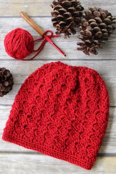 a red crocheted hat sitting on top of a wooden table next to pine cones