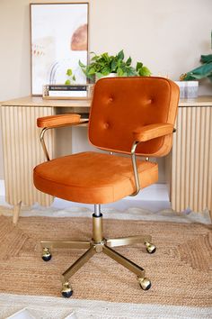 an orange office chair sits in front of a desk with a potted plant on it