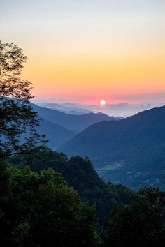 the sun is setting in the distance over some hills and valleys with trees on either side