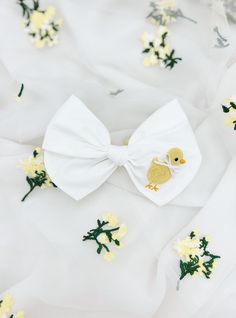 White cotton medium bow with an embordered baby chick.  Length: 5 inches  Finish: Clip or Nylon Headband Cute Satin Bow For Spring, Cute White Bow With Ribbon, Cute White Ribbon Bow, White Summer Bow For Gifts, White Ribbon Bow For Spring, Cute Summer Bow With Ribbon, Cute Spring Bow For Gift, Cotton Bow For Spring, Spring Cute Butterfly Knot Bow