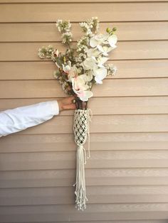 a bouquet of flowers hanging from the side of a house with someone's hand holding it