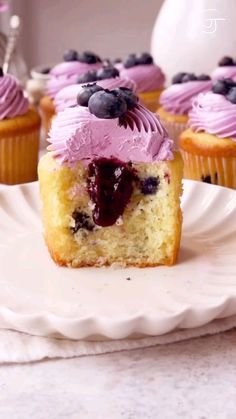 cupcakes with purple frosting and blueberries on top are sitting on a white plate