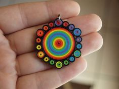 a hand holding a colorful pendant in it's left hand with an orange, blue, green, yellow and red circle on it