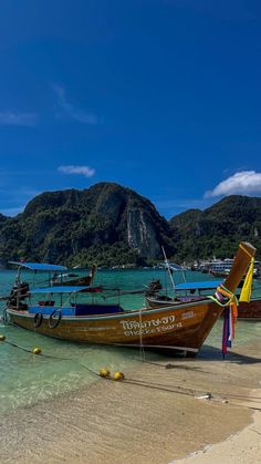 two boats on the beach with mountains in the backgrouds and clear blue water