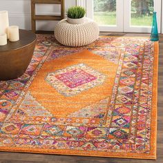 an orange area rug in front of a window with candles on the table and vase