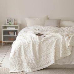 an unmade bed with white sheets and blankets on it, next to a night stand