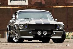 an old muscle car parked in front of a rusted building