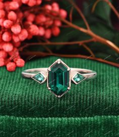 an emerald colored stone ring sitting on top of a green cloth next to red berries