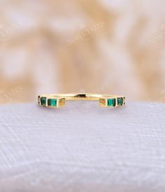 a gold ring with emeralds on it sits on a white cloth surface in front of a beige background