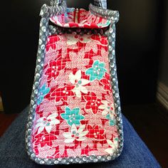 a red and blue purse sitting on top of a denim chair next to a black wall