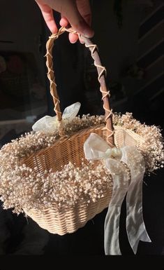 a person holding a wicker basket with flowers and ribbons on the handle, in front of a black background