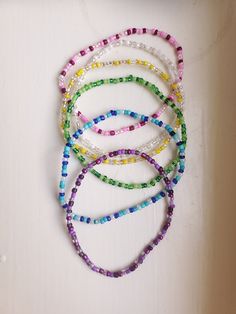 four bracelets with different colored beads are on a white surface and one is in the shape of a heart