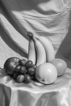 black and white photograph of bananas, apples, and oranges on a table cloth