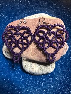 two heart shaped purple beads are on top of a rock and one is attached to a pair of earrings