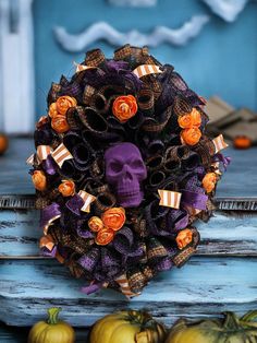 a wreath decorated with orange and purple decorations on top of a blue table next to pumpkins