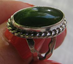 This is a very striking and colorful ring with no maker or metal markings. It looks like green jade. The face of the ring measures 3/4" from top to bottom and 7/16" across. It has a beautiful braided mount and split shank. This ring rests between a 5 and a 5.25 on a mandrel. The ring weighs  4.6 grams. Great eye appeal! Green Oval Cabochon Ring For Gift, Handmade Green Oval Cabochon Ring, Handmade Oval Green Ring, Handmade Green Oval Ring, Green Oval Cabochon Emerald Ring Collectible, Handmade Green Emerald Oval Cabochon Ring, Unique Oval Jade Rings, Unique Green Oval Cabochon Jewelry, Hand Accessories