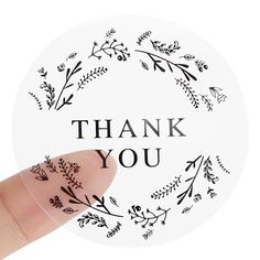 a hand holding up a sticker with the words thank you written in black on it