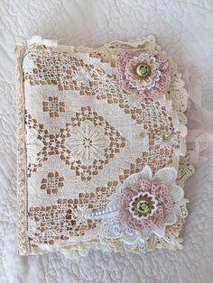 an old doily with flowers on it laying on a white bed sheet and lace